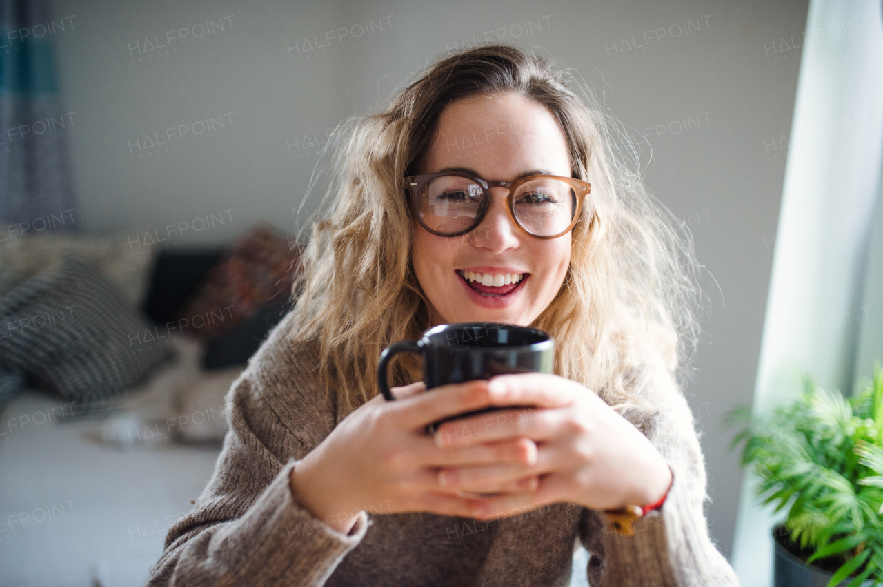 Front view of young woman relaxing indoors at home with cup of coffee or tea.