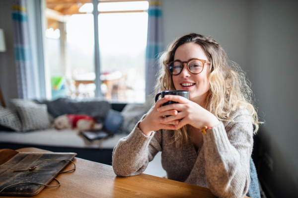 Front view of young woman relaxing indoors at home with cup of coffee or tea.