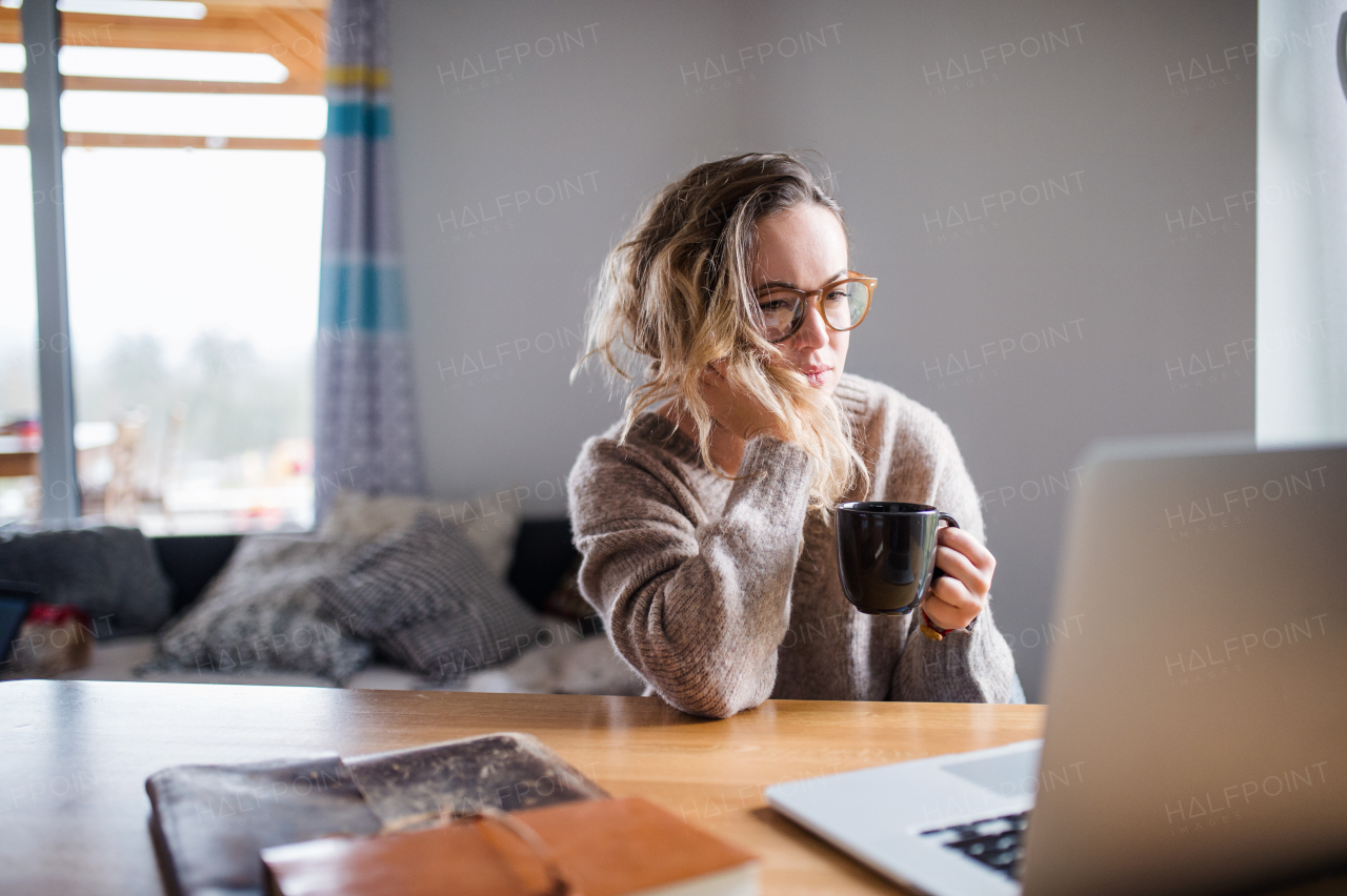 Portrait of young woman with laptop and coffee working indoors at home.