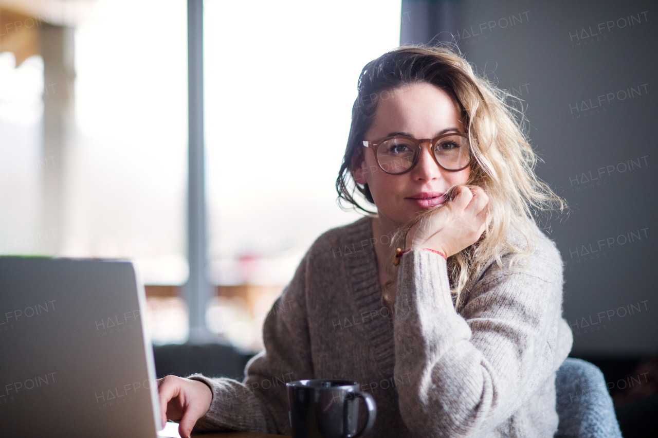 Portrait of young woman with laptop and coffee relaxing indoors at home.