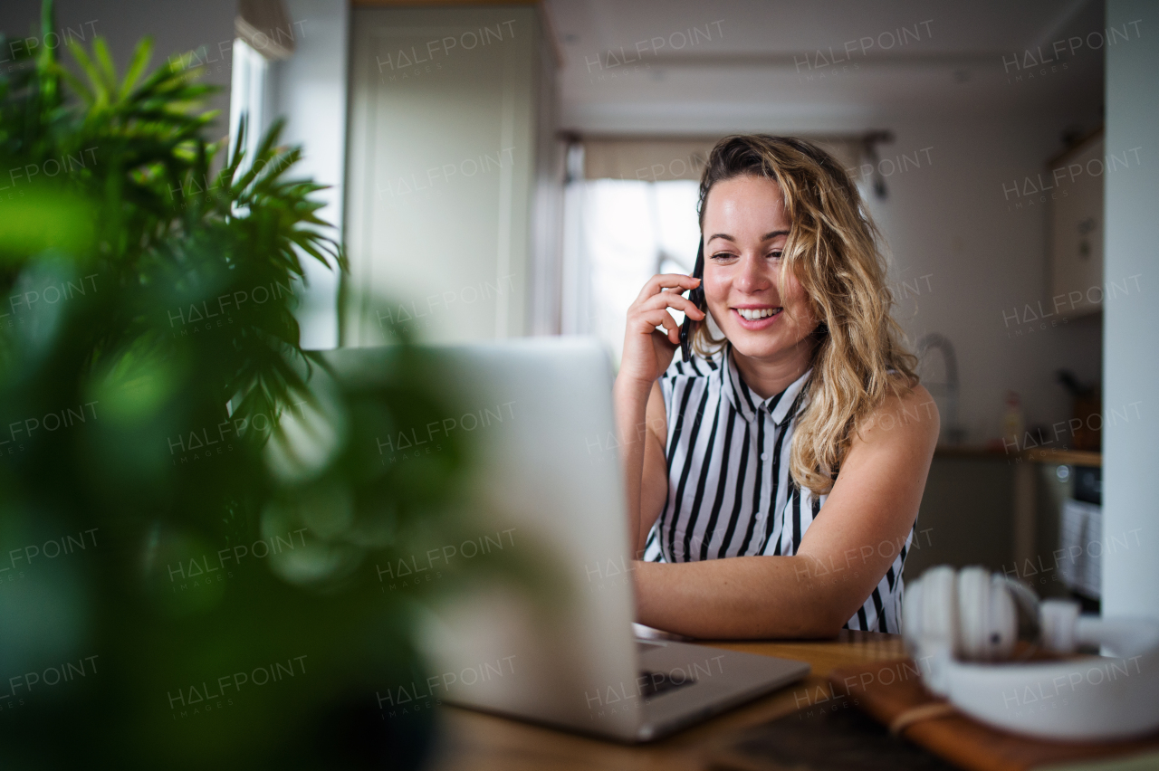 Portrait of young woman with laptop and smartphone working indoors at home.