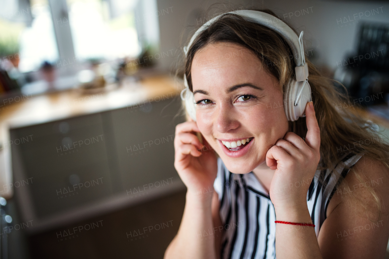 Happy young woman with headphones relaxing indoors at home, listening to music.