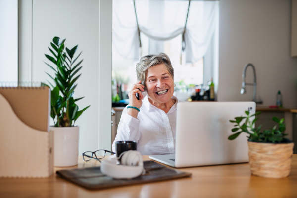 Portrait of senior woman with laptop and smartphone working in home office.