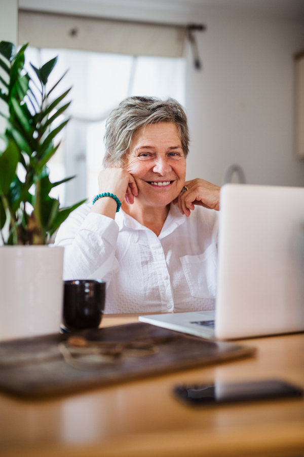 Portrait of senior woman with laptop and smartphone working in home office.