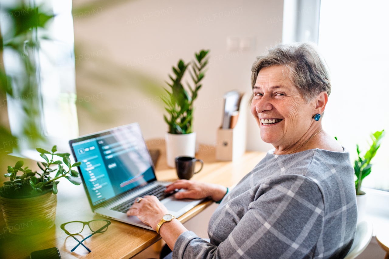 Portrait of senior woman with laptop working in home office, looking at camera.