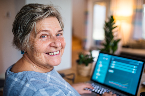 Portrait of senior woman with laptop working in home office, looking at camera.