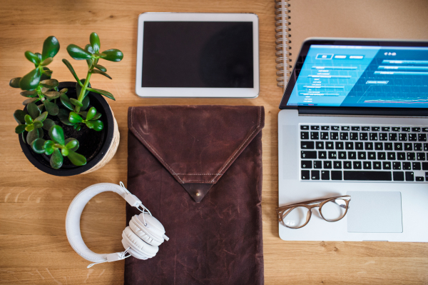 Composition of tablet, laptop, headphones and potted plant on desk, top view.