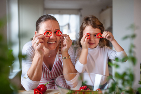 Small girl with senior grandmother in kitchen indoors at home, having fun when cooking.