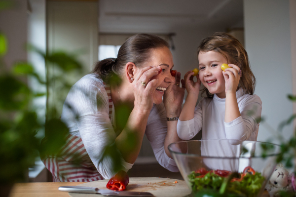 Small girl with senior grandmother in kitchen indoors at home, having fun when cooking.