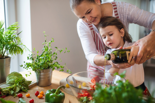 Small girl with senior grandmother in kitchen indoors at home, making vegetable salad.