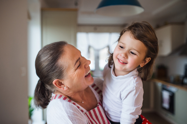 Happy small girl with senior grandmother in kitchen indoors at home.