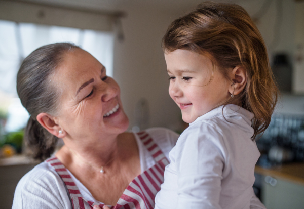 Happy small girl with senior grandmother in kitchen indoors at home.