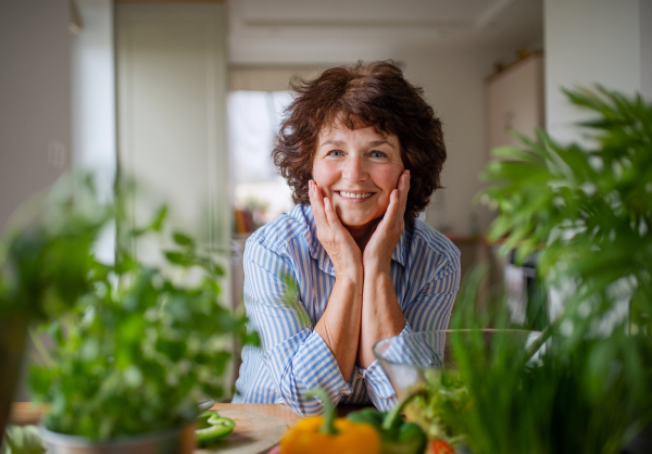 Senior woman preparing food in kitchen at home, looking at camera.