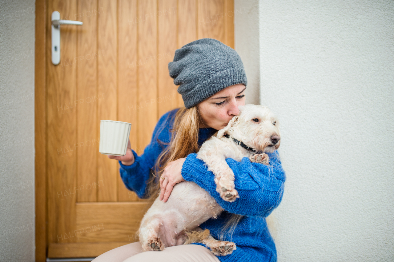 Mature woman relaxing outdoors by front door at home with coffee and pet dog. Copy space.