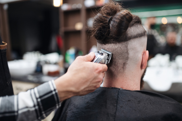 A rear view of man client visiting haidresser in barber shop.