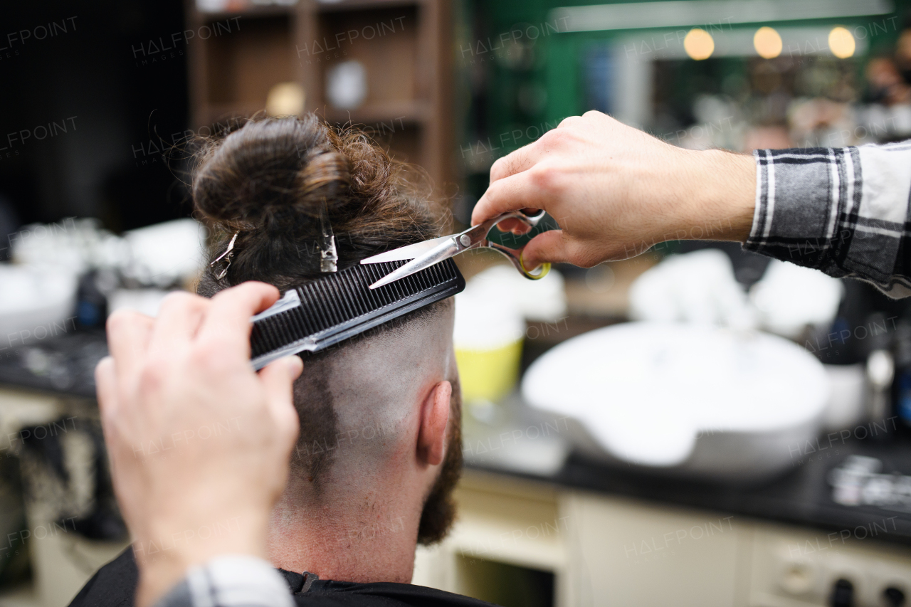 A rear view of man client visiting haidresser in barber shop.