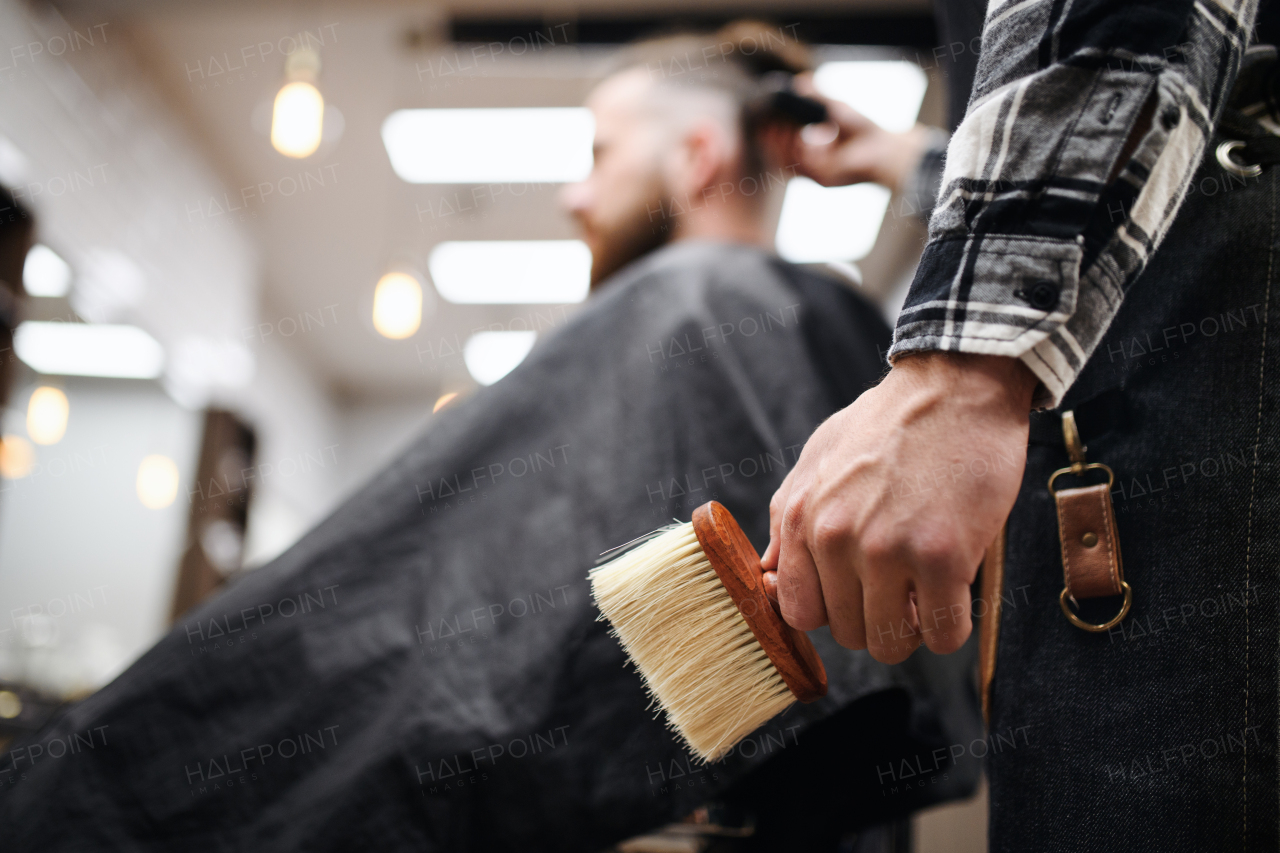 Young man client in barber shop, unrecognizable barber holding brush.