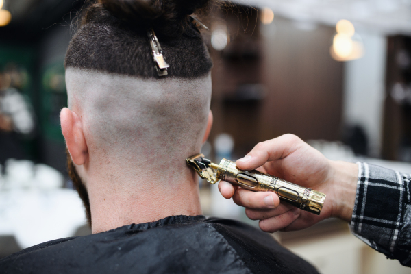 A rear view of man client visiting haidresser in barber shop.