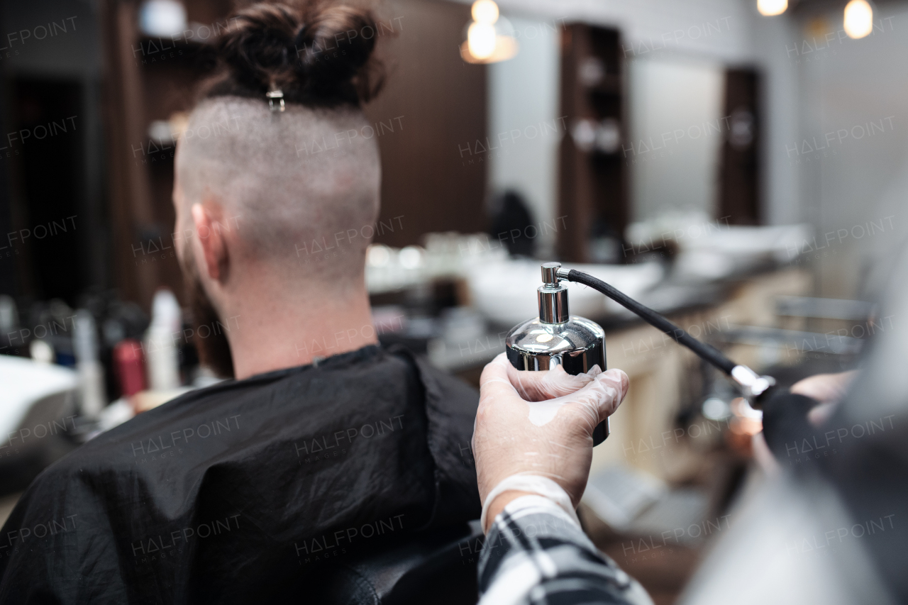 A rear view of man client visiting haidresser in barber shop.