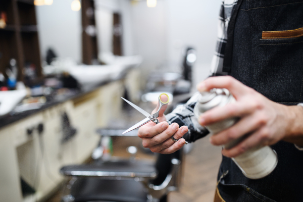 An unrecognizable man haidresser disinfecting scissors in barber shop, coronavirus and new normal concept.