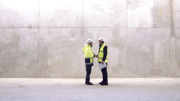 Two men engineers standing on construction site, shaking hands and talking.