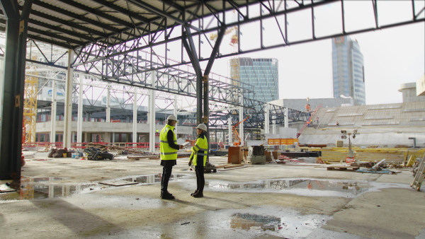 Mature man and woman engineers standing on construction site, talking.