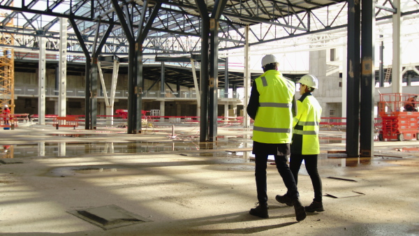 Rear view of man and woman engineers walking on construction site, talking.