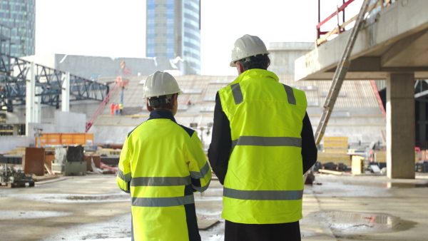 Rear view of man and woman engineers walking on construction site, talking.