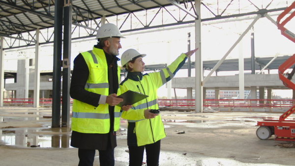 Man and woman engineers with walkie talkie standing on construction site, talking.