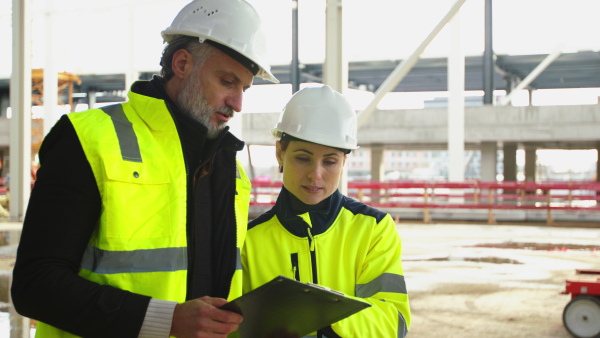 Mature man and woman engineers standing on construction site, talking.