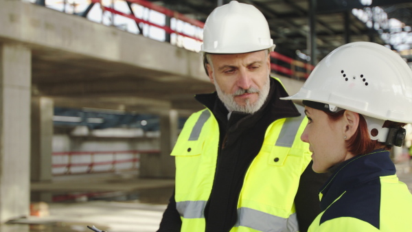 Mature man and woman engineers standing on construction site, talking.