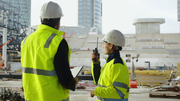 Man and woman engineers with walkie talkie standing on construction site, talking.