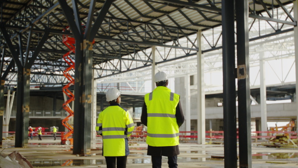 Rear view of man and woman engineers walking on construction site, talking.