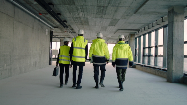 A rear view of group of engineers walking on construction site, talking.