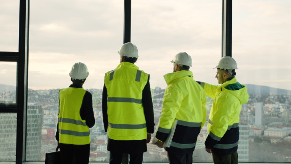 Rear view of group of engineers standing on construction site, talking.