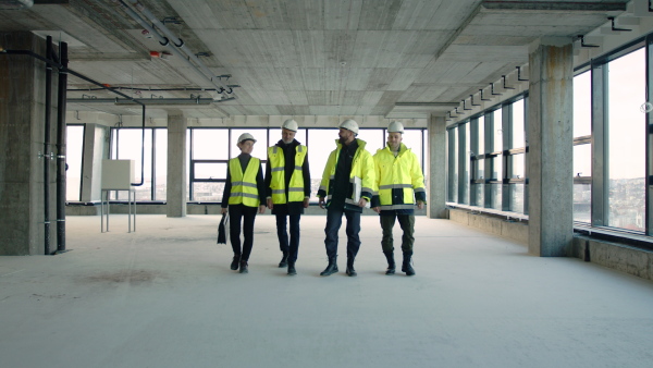 Front view of group of engineers walking on construction site, talking.