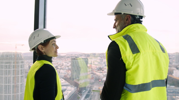 Mature man and woman engineers on construction site, talking.