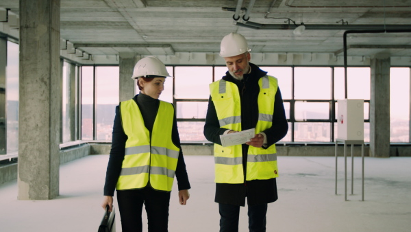 Front view of man and woman engineers walking on construction site, talking.