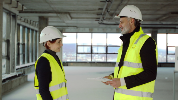 Mature man and woman engineers standing on construction site, talking.