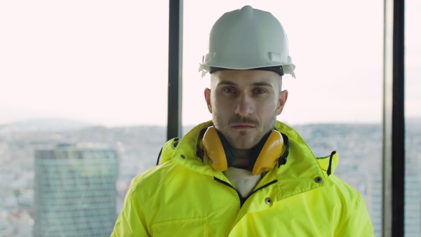 Front view of young engineer standing on construction site, looking at camera.