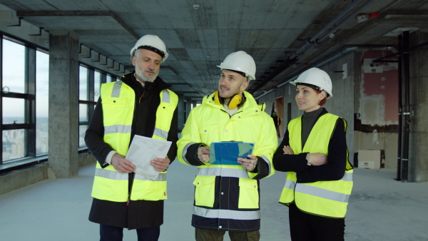 Front view of group of engineers with blueprints standing on construction site, talking.