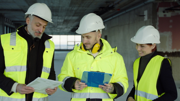 Front view of group of engineers with blueprints standing on construction site, talking.