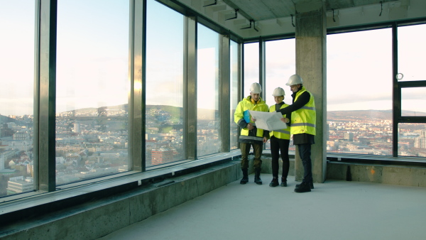 Front view of group of engineers with blueprints standing indoors on construction site, talking.