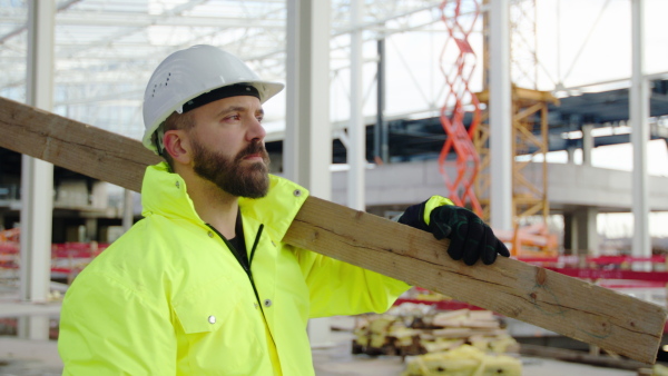 Man worker standing outdoors on construction site, carrying wooden beam.