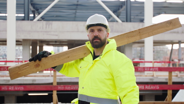 Front view of mature man worker standing outdoors on construction site, holding beam.