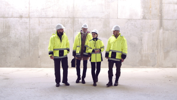 Front view of group of engineers walking on construction site, talking.