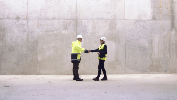 Two men engineers standing on construction site, shaking hands and talking.