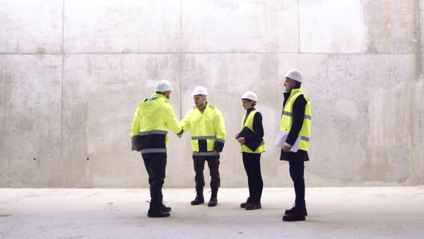 A group of engineers standing on construction site, shaking hands. Copy space.