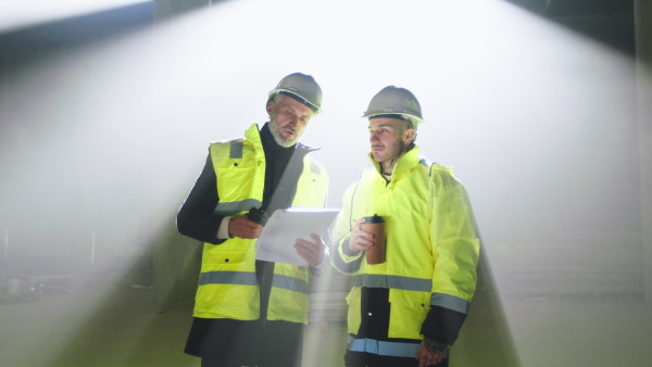 Front view of men engineers with walkie talkie standing on construction site, talking.