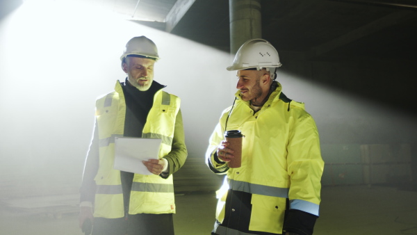 Front view of men engineers with walkie talkie standing on construction site, talking.